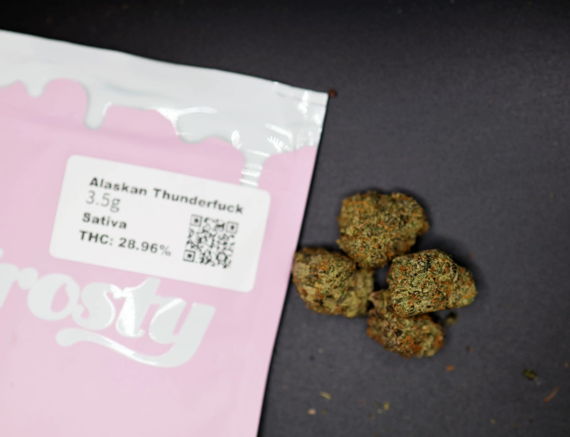 Pink packaging of Alaskan Thunderfuck thca flower with visible text and branding on a dark surface.