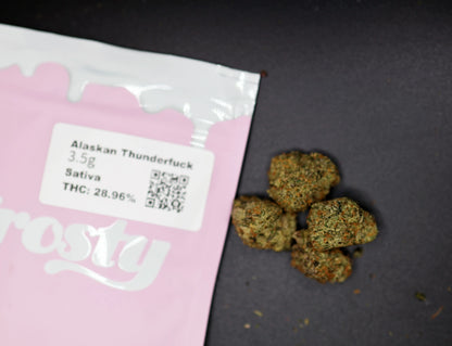 Pink packaging of Alaskan Thunderfuck thca flower with visible text and branding on a dark surface.