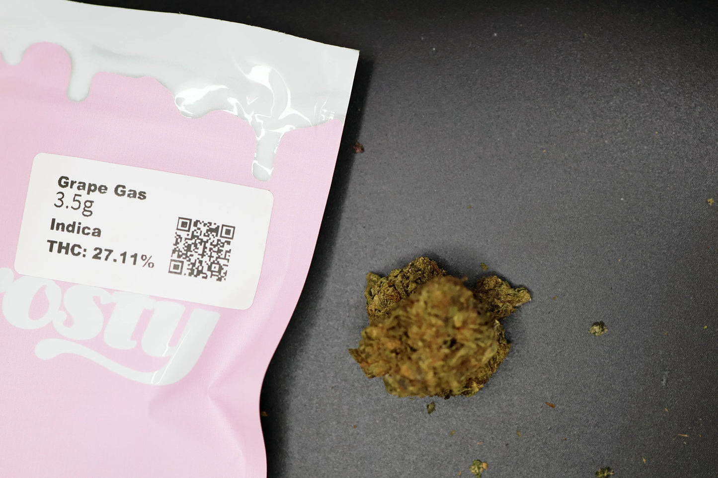 Pink packaging with a label for 'Grape Gas' cannabis product on a dark surface with grape gas indica flower 