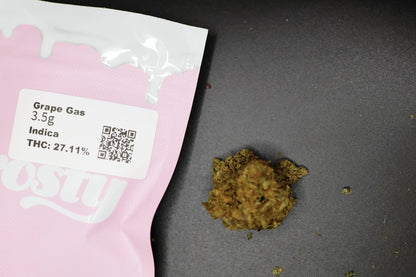 Pink packaging with a label for 'Grape Gas' cannabis product on a dark surface with grape gas indica flower 