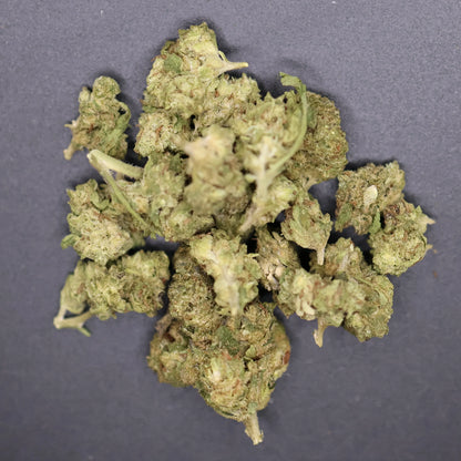 close up of pile of green crack smalls thca buds on a flat dark surface