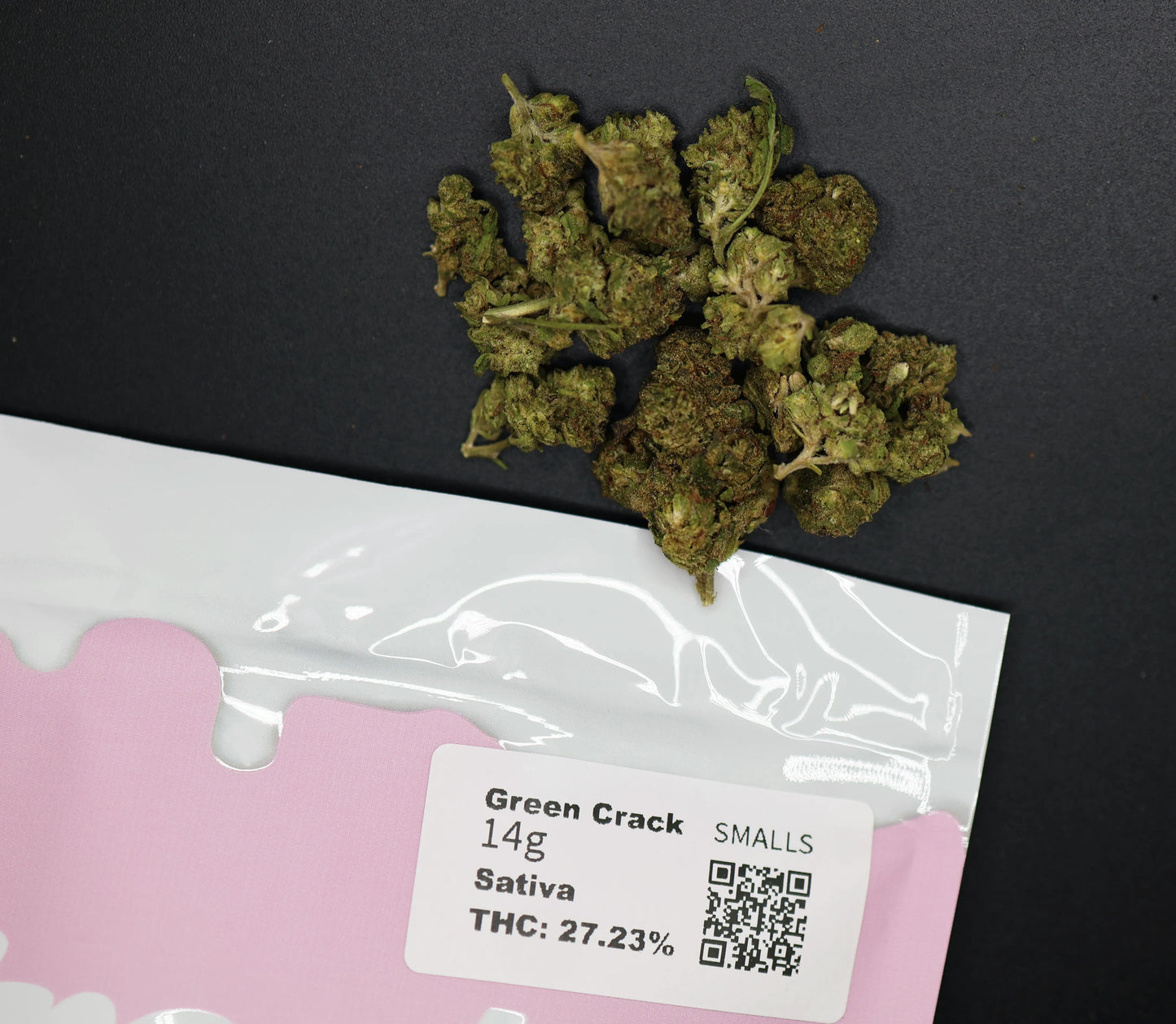 Dried cannabis buds on a pink packaging with a green crack smalls label on a black background